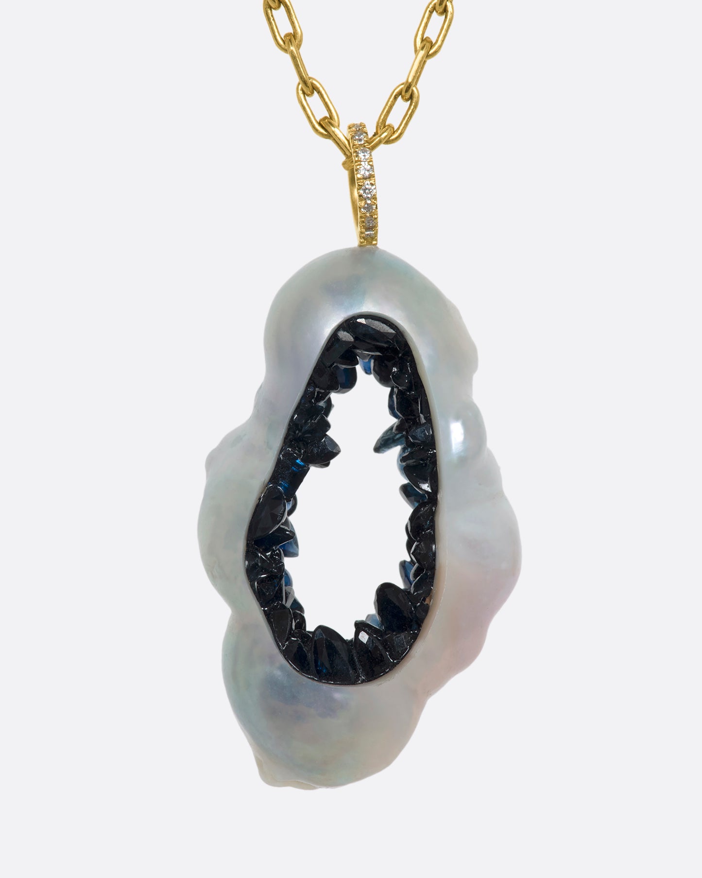 A yellow gold necklace with a hollowed souffle pearl pendant filled with a blue sapphire geode hanging from a pave diamond bale. Shown from the front.