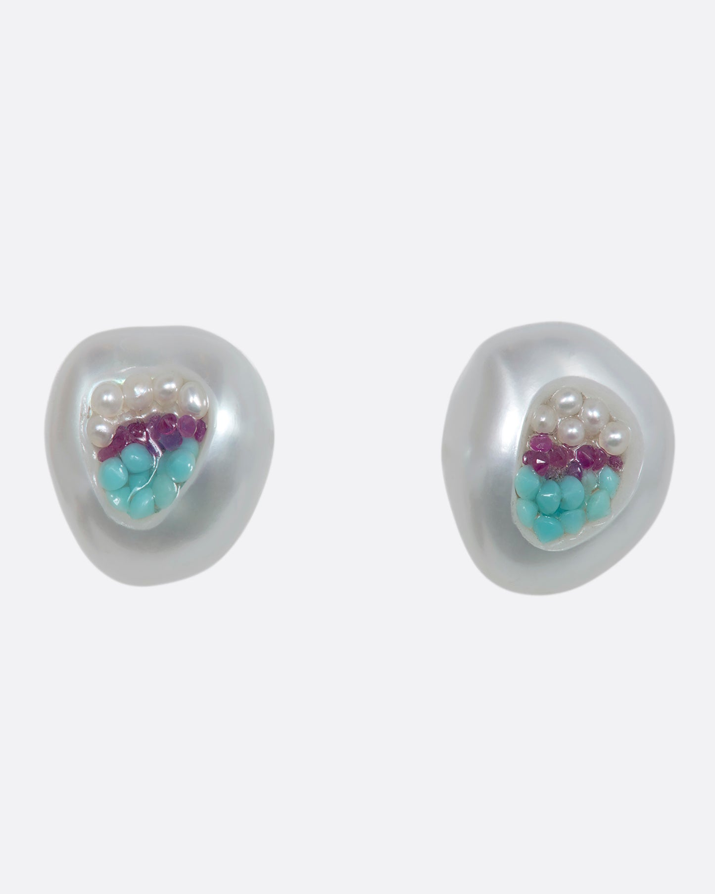 A pair of hollow pearl studs filled with seed pearls, turquoise and rubies. Shown from the front.