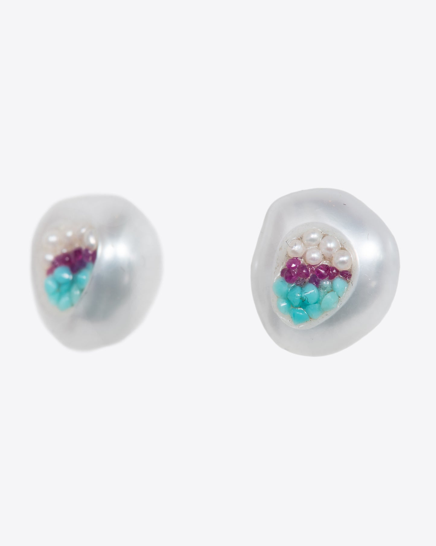 A pair of hollow pearl studs filled with seed pearls, turquoise and rubies. Shown from the side.