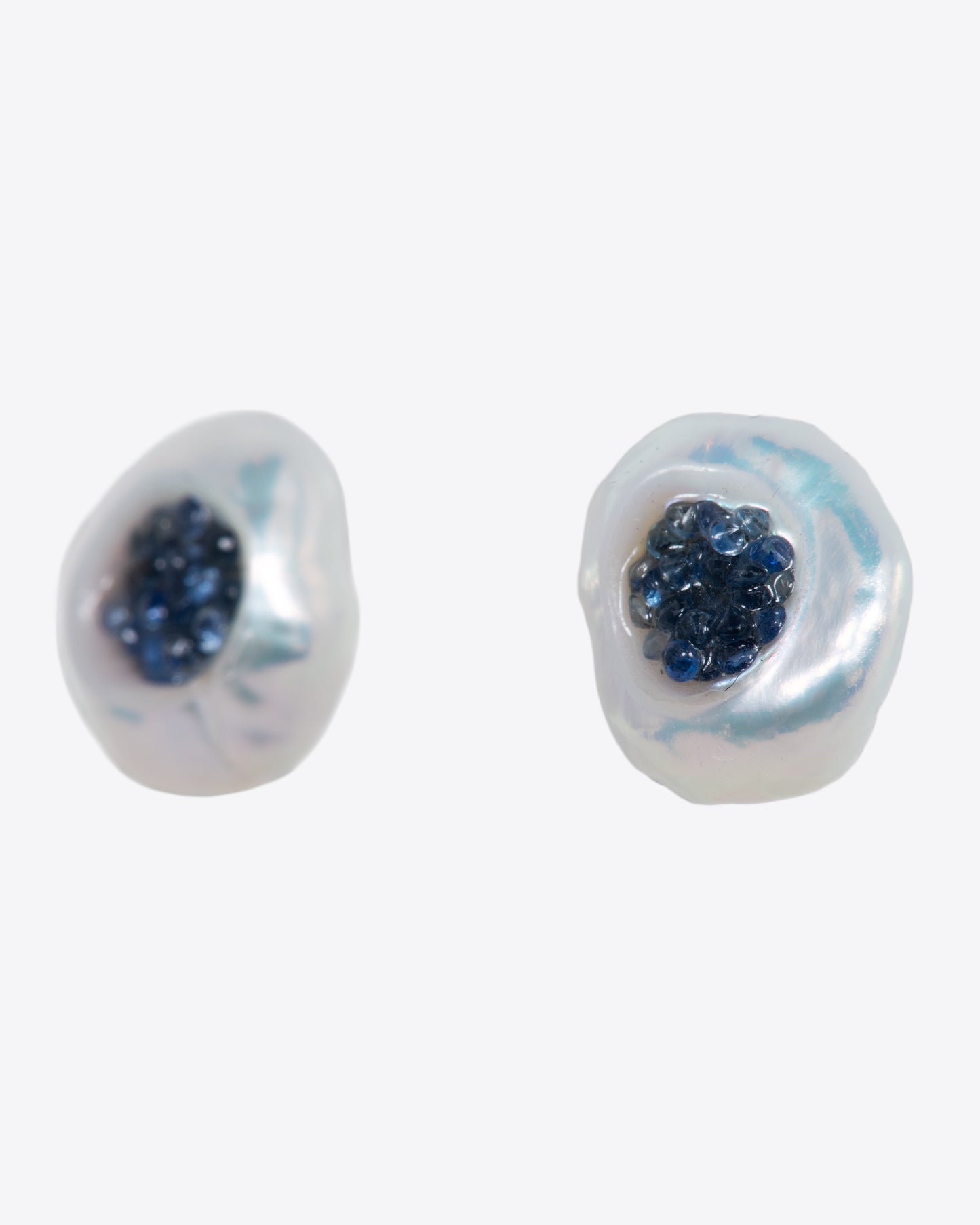 A pair of yellow gold earrings with hollowed out pearls filled with sapphires. Shown from the side.