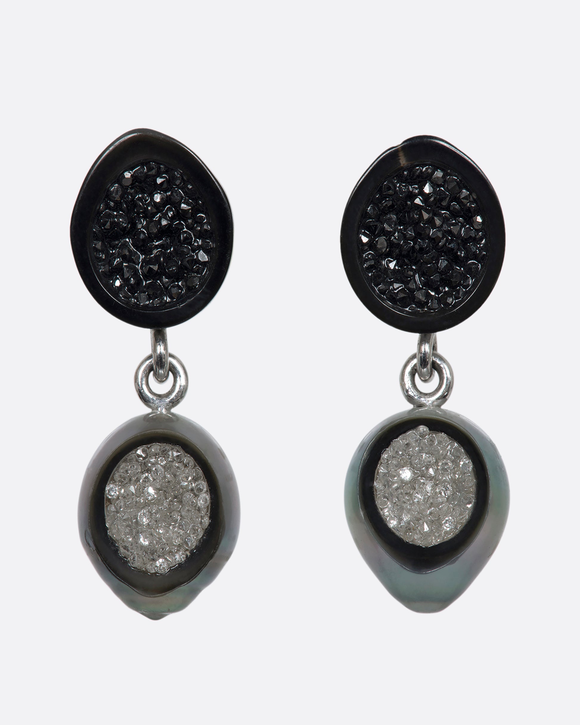 A pair of white gold hollowed out pearl drop earrings with black and white diamonds filling each. Shown from the front.