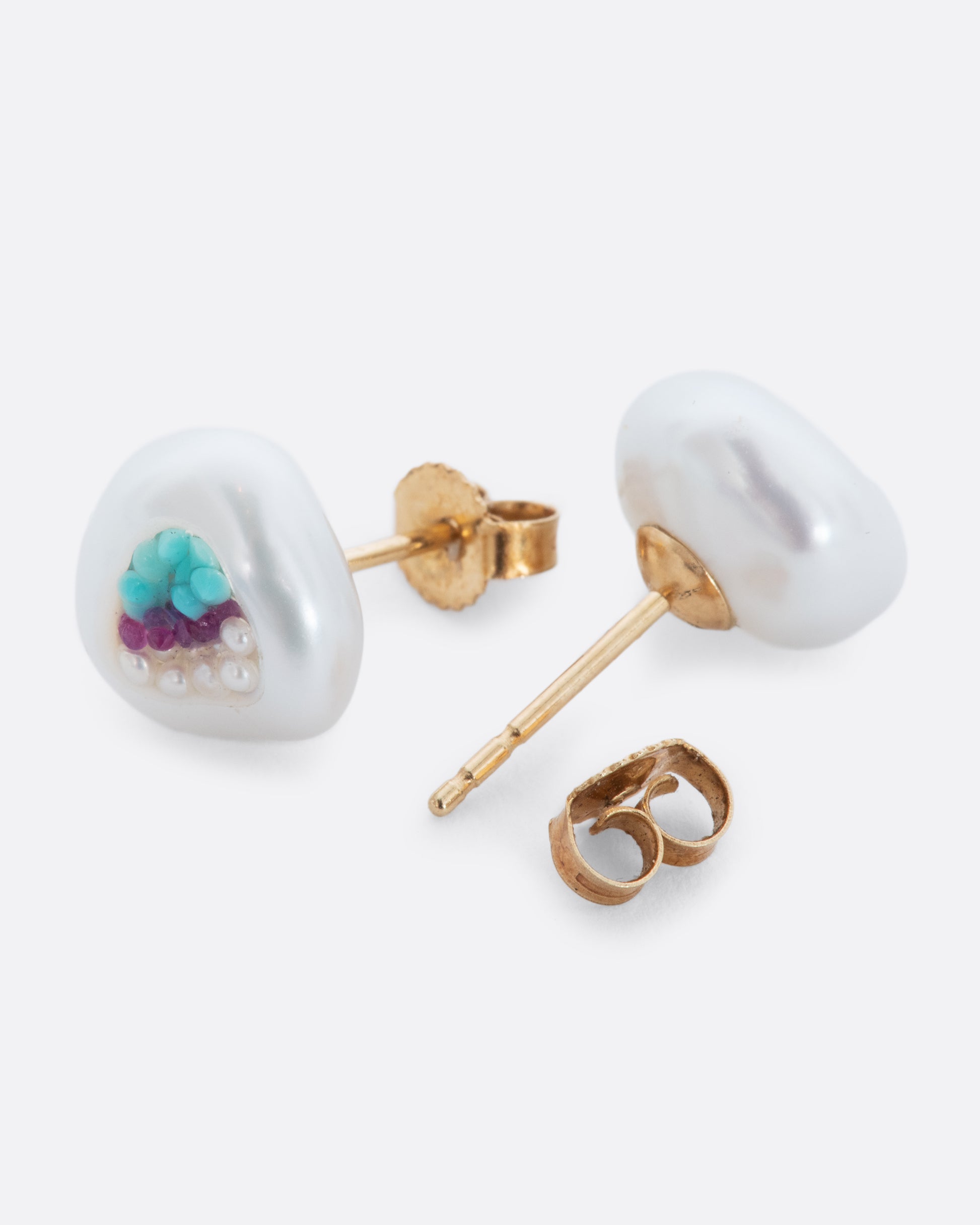 A pair of hollow pearl studs filled with seed pearls, turquoise and rubies. Shown from the front and back alternating.