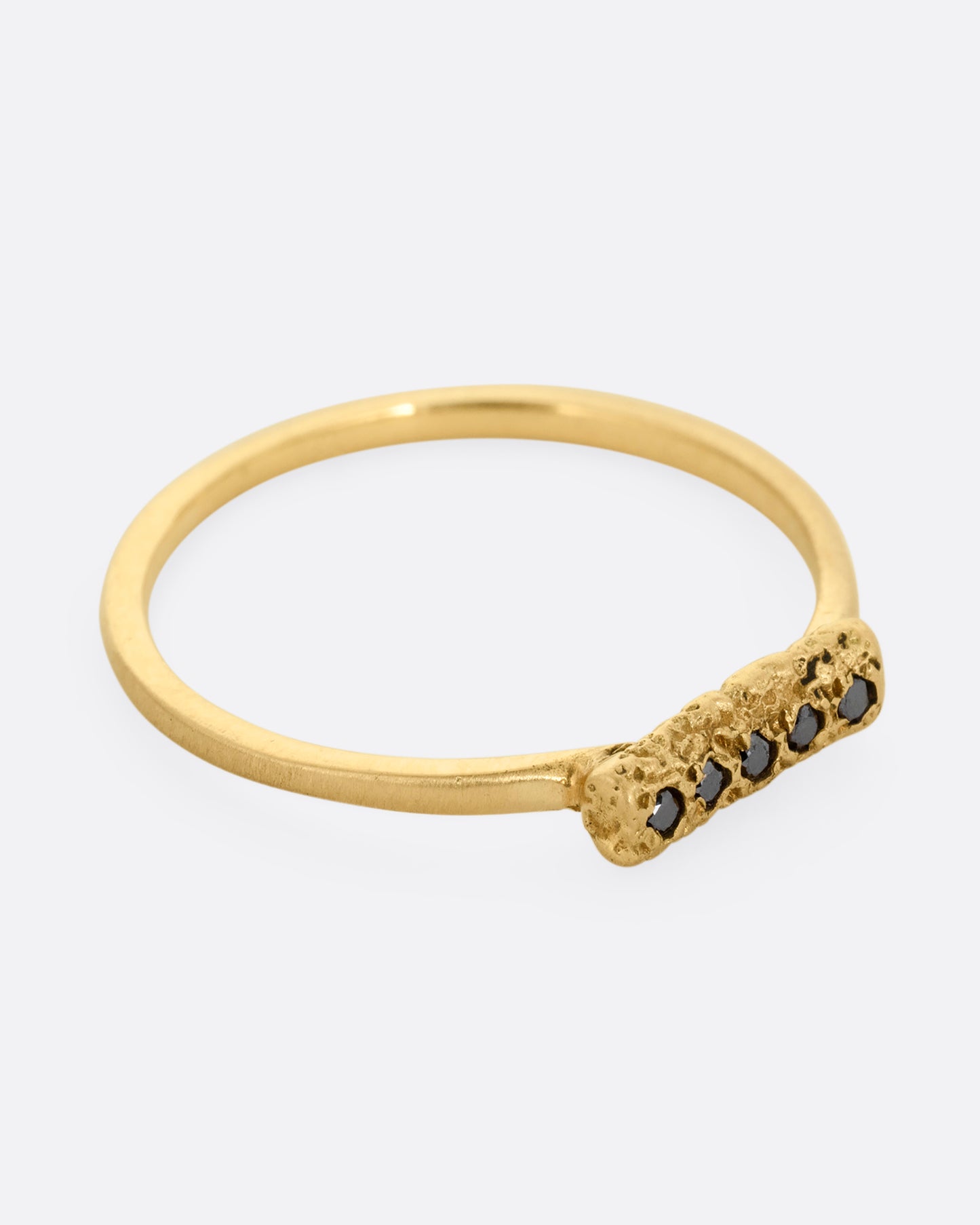 A yellow gold ring with five black diamonds set in a textured rectangular face. Shown from the side.