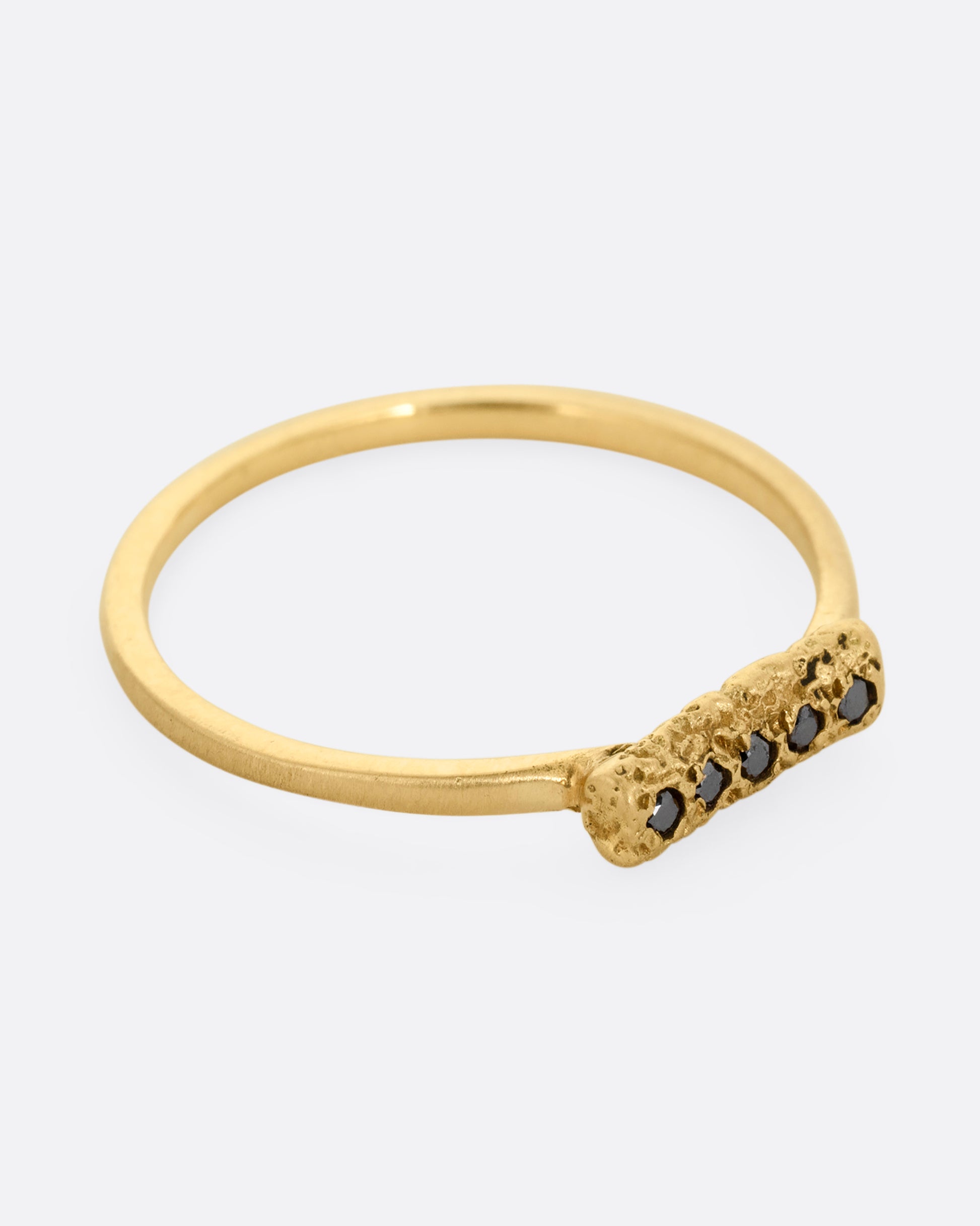 A yellow gold ring with five black diamonds set in a textured rectangular face. Shown from the side.
