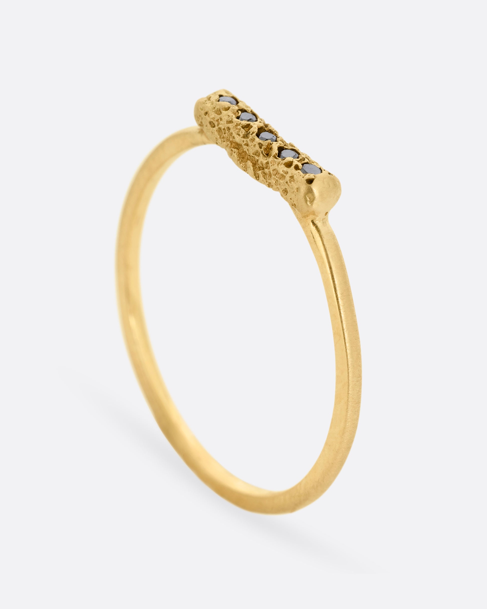 A yellow gold ring with five black diamonds set in a textured rectangular face. Shown from the side standing up.