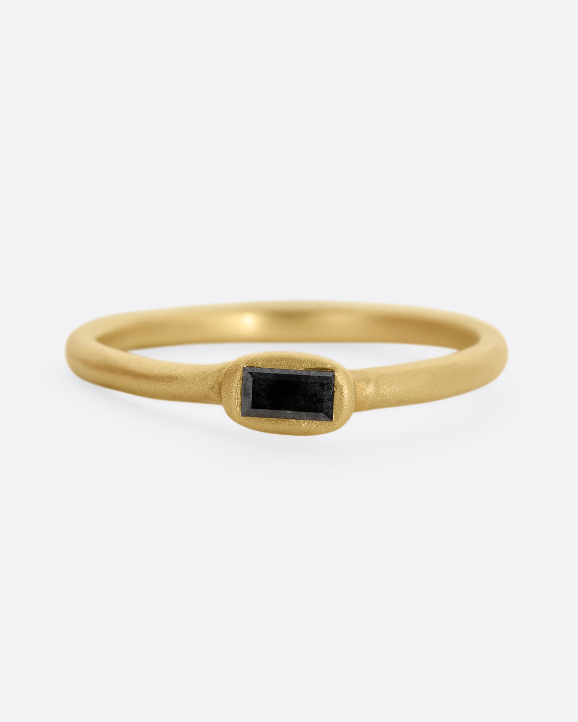 A yellow gold ring with a horizontally set salt and pepper baguette diamond, shown from the front.