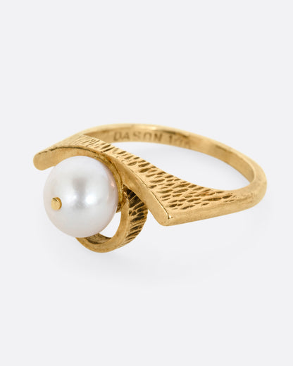 A yellow gold ring with a white pearl shown from the side.