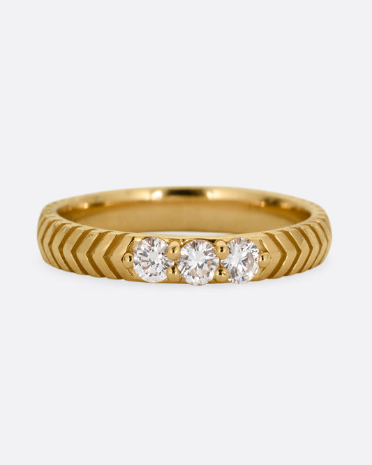 A yellow gold ring with arrow etching and three white diamonds. Shown from the front.