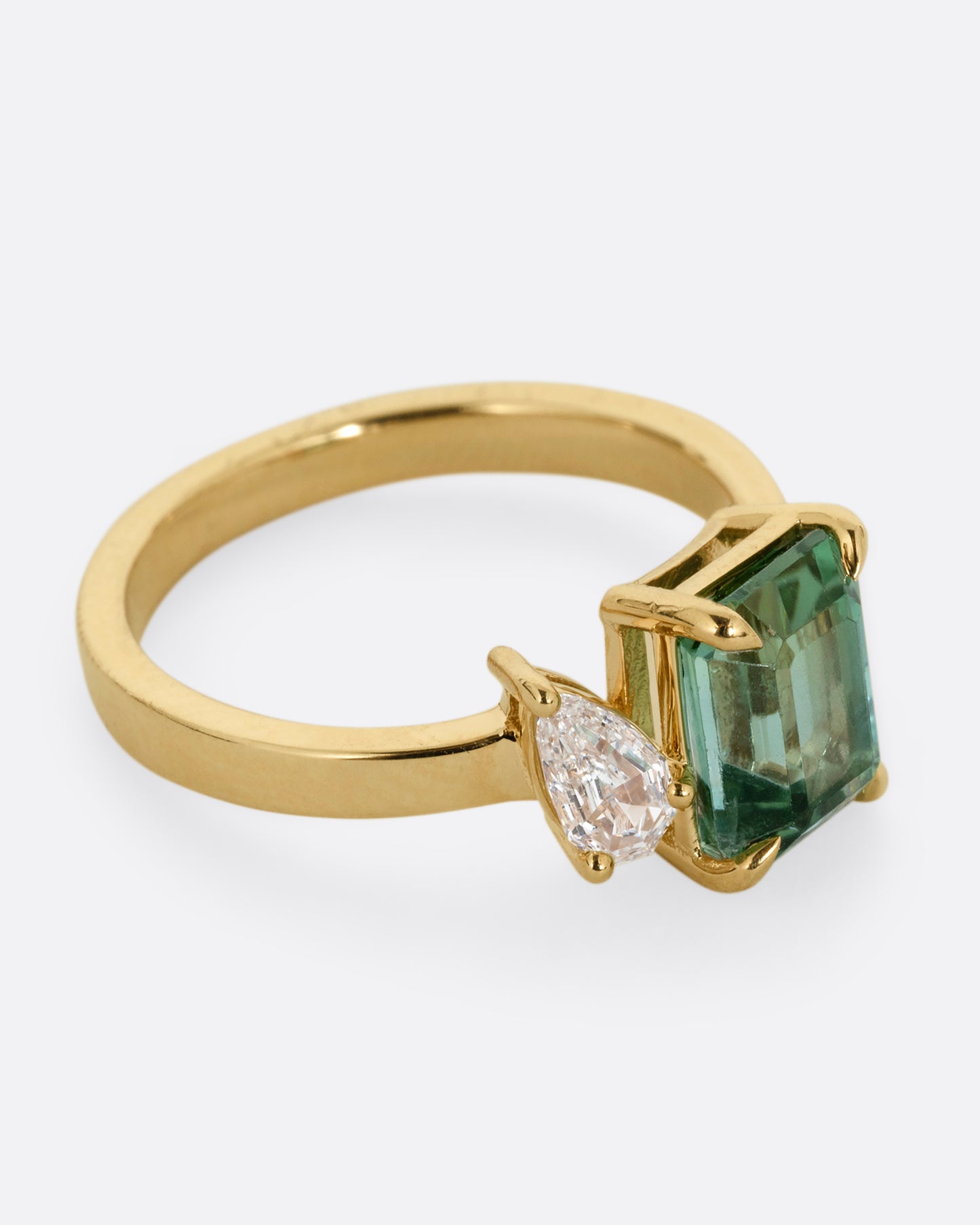 A yellow gold ring with a green tourmaline and pear cut diamond, shown from the side.