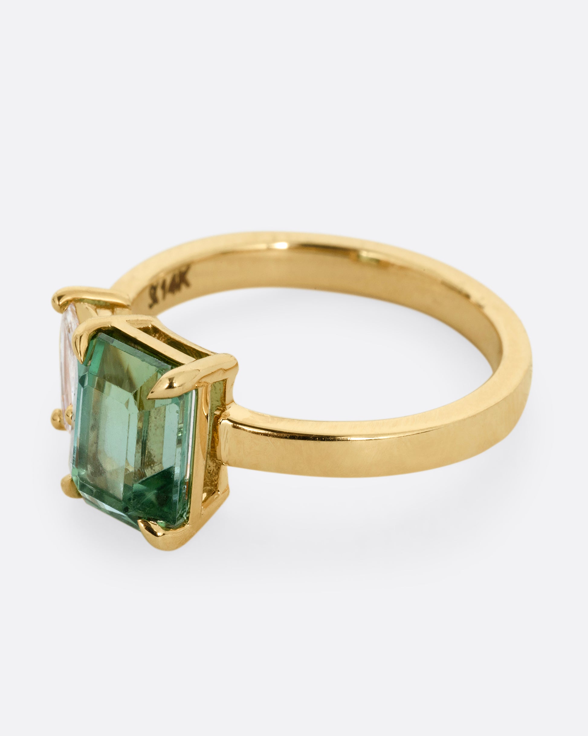 A yellow gold ring with a green tourmaline and pear cut diamond, shown from the side.