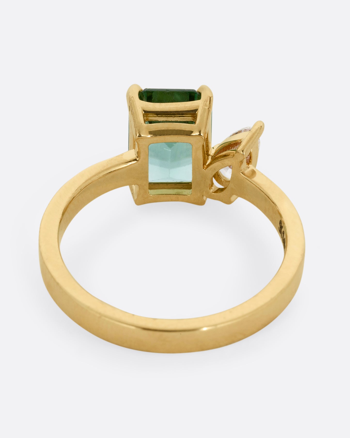 A yellow gold ring with a green tourmaline and pear cut diamond, shown from the back.