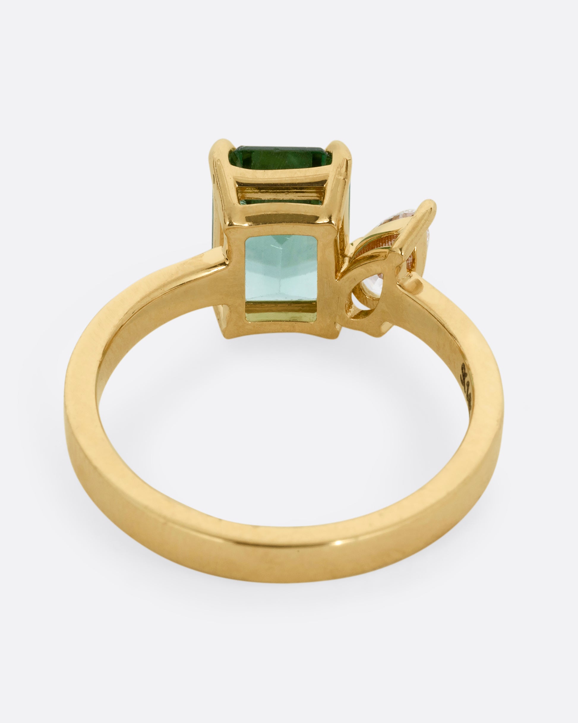 A yellow gold ring with a green tourmaline and pear cut diamond, shown from the back.