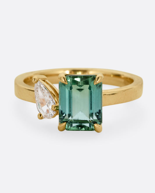 A yellow gold ring with a green tourmaline and pear cut diamond, shown from the front.