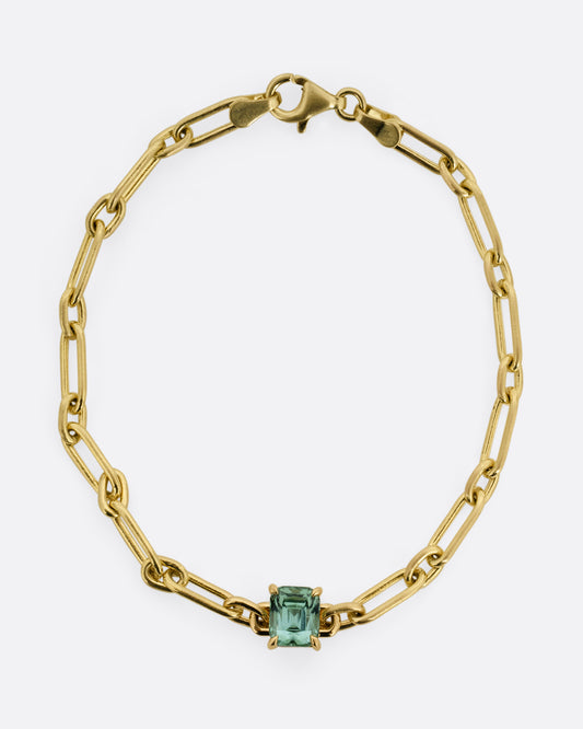 A yellow gold chain link bracelet with a  prong set aqua tourmaline at the center. Shown from the front.