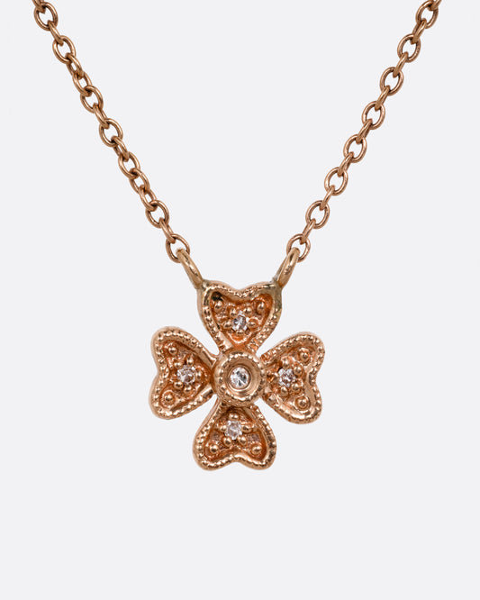 A rose gold cable chain necklace with a diamond studded four leaf clover charm at the center. Shown from the front.
