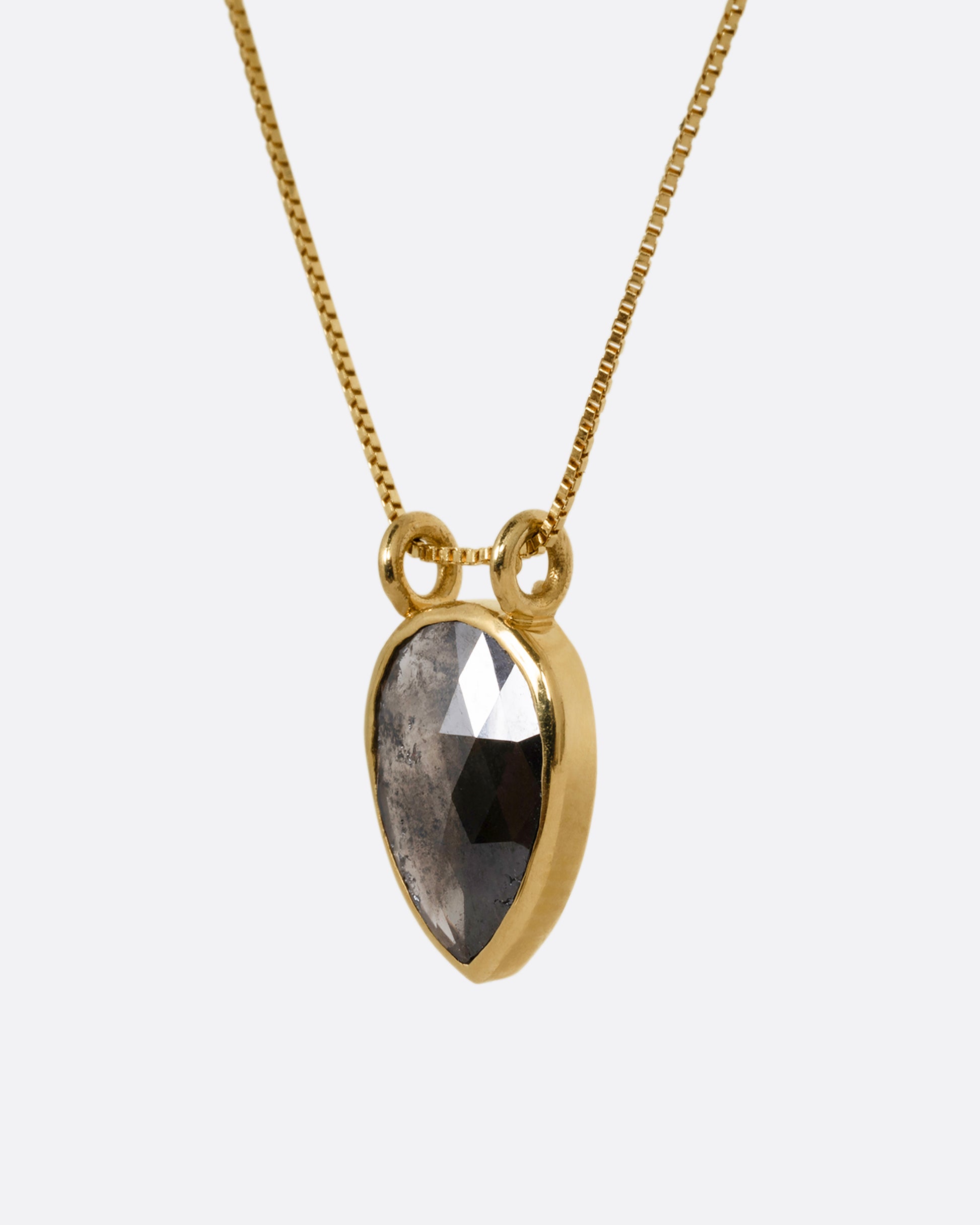 A yellow gold box chain necklace with a pear shaped salt and pepper diamond pendant shown from the side.