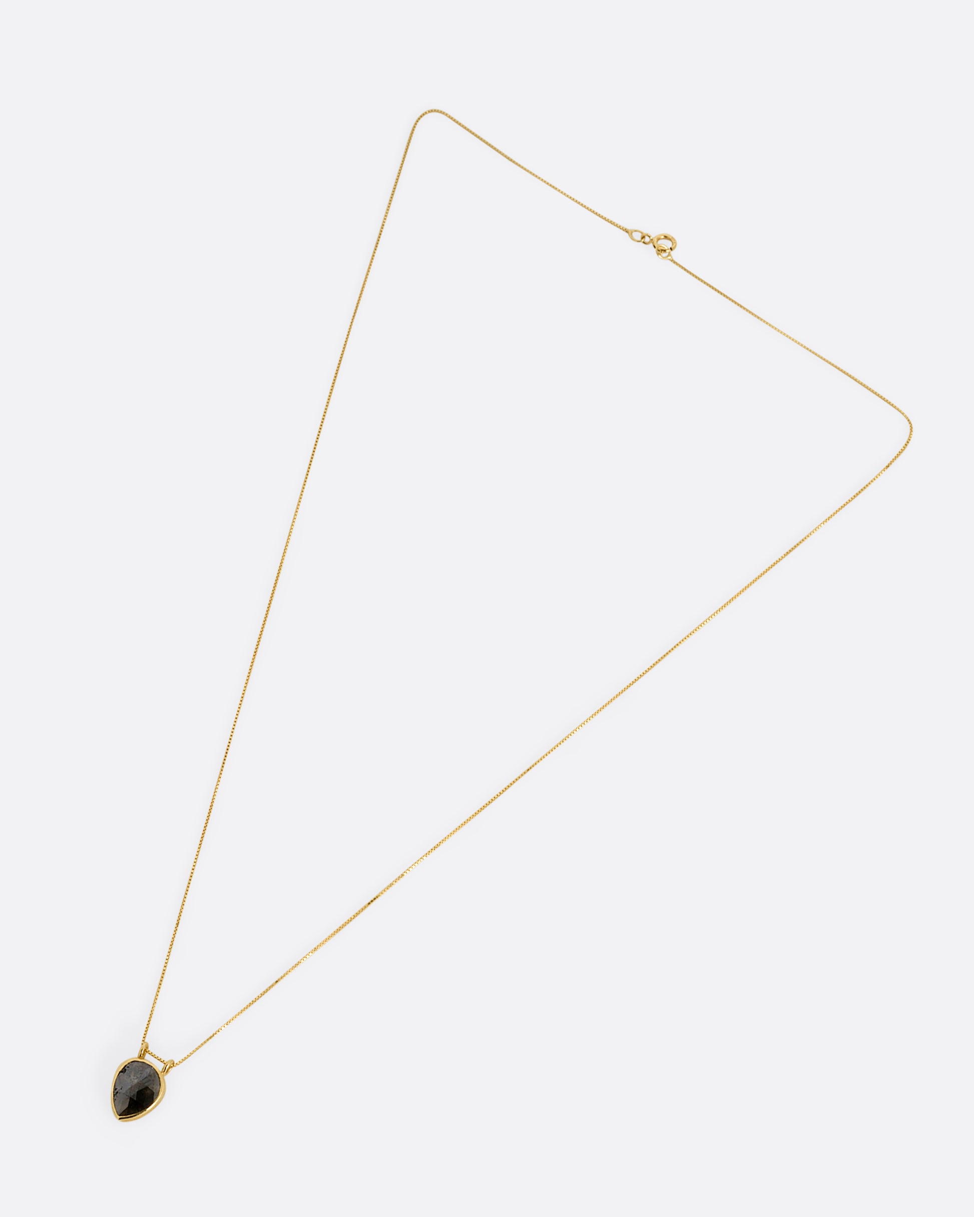 A yellow gold box chain necklace with a pear shaped salt and pepper diamond pendant shown from the front.