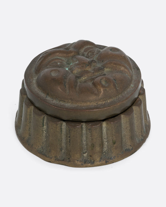 A round box with a face on the lid and ridged sides. Shown from the front.