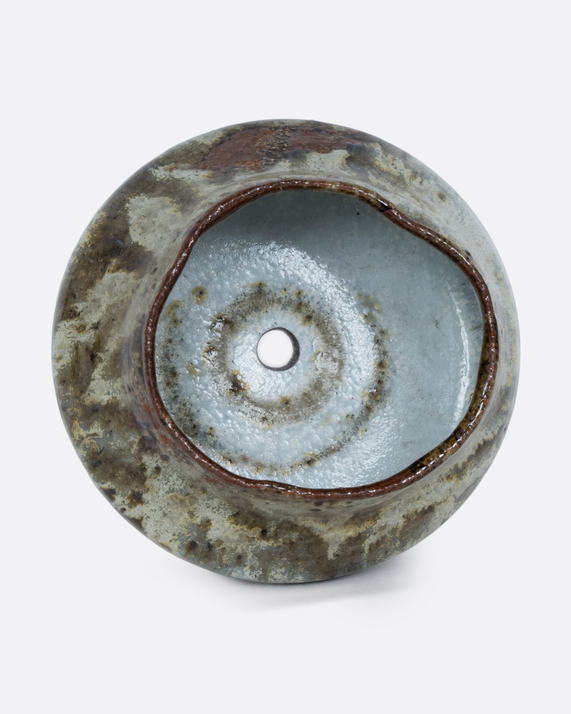 This ceramic planter with a green marbled glaze and drainage hole. Shown on its side from the top.