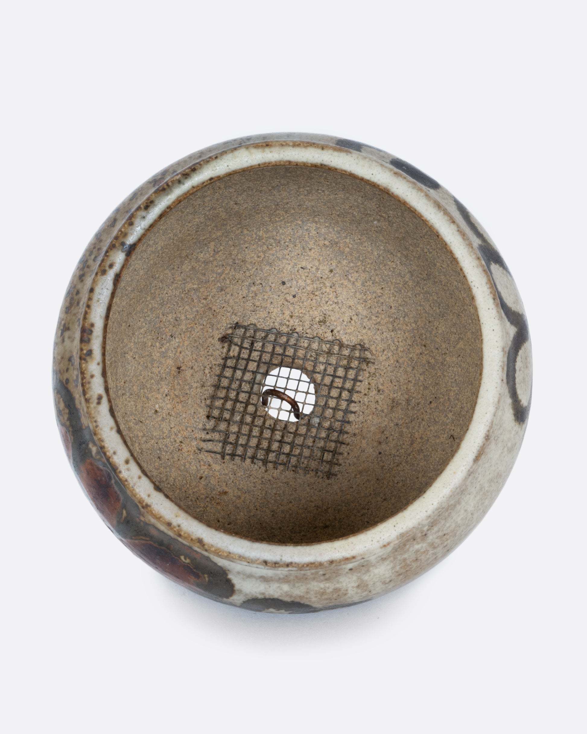 A pot with a brown handpainted pattern of flowers and a drainage hole at its base. Shown from the top.