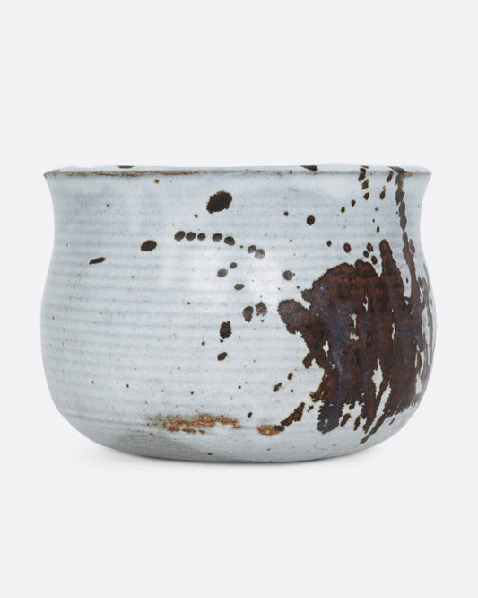 A white pot with a brown splattered glaze and a drainage hole at its base. Shown from the front.
