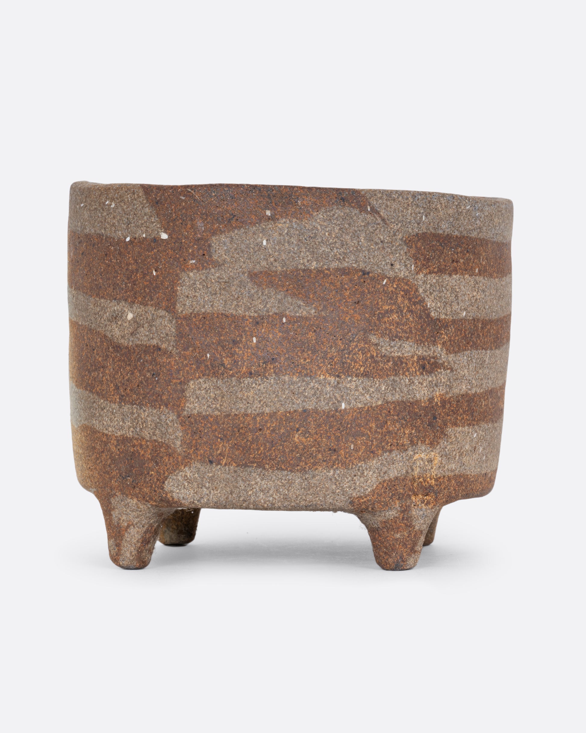 A brown ceramic footed pot with an all over geometric pattern and drainage hole. Shown from the side.
