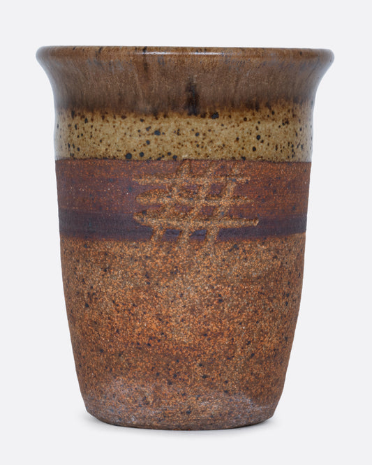 A striped brown pot with a hatched etching, a drainage hole at its base, and a textural finish.
