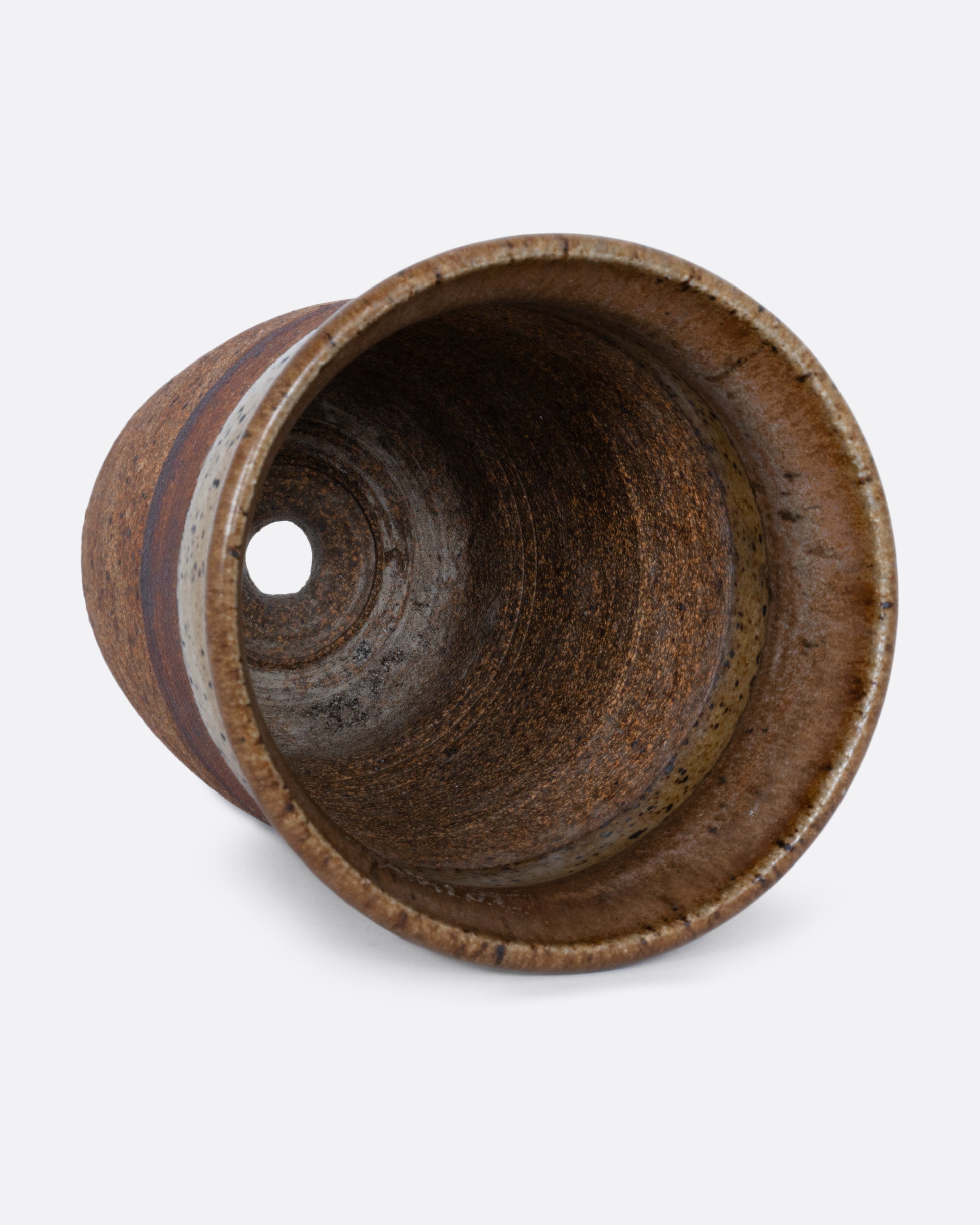 A striped brown pot with a hatched etching, a drainage hole at its base, and a textural finish. Shown lying on its side from the top.