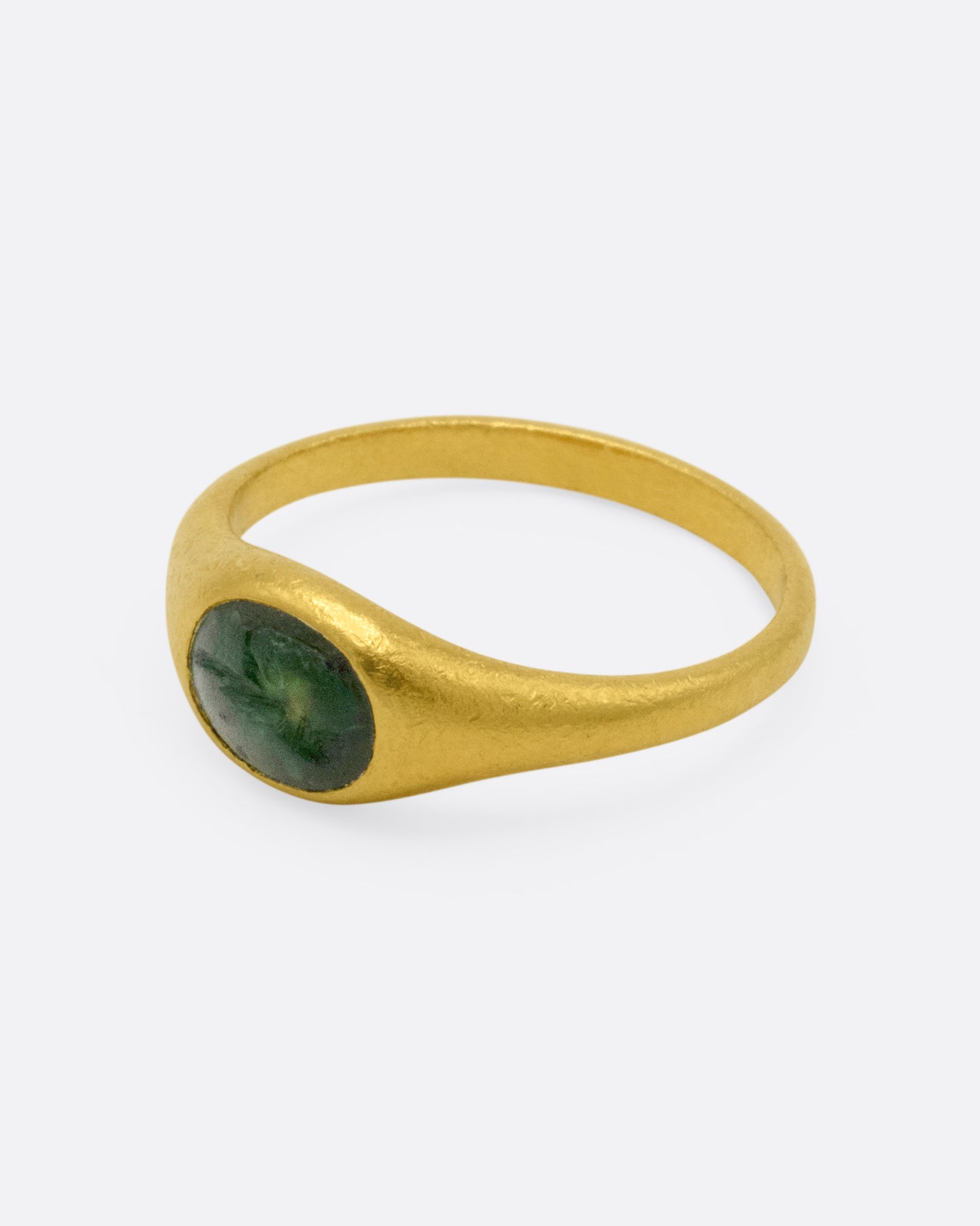 A yellow gold signet ring with a dark green chalcedony carved with a parrot, shown from the side.