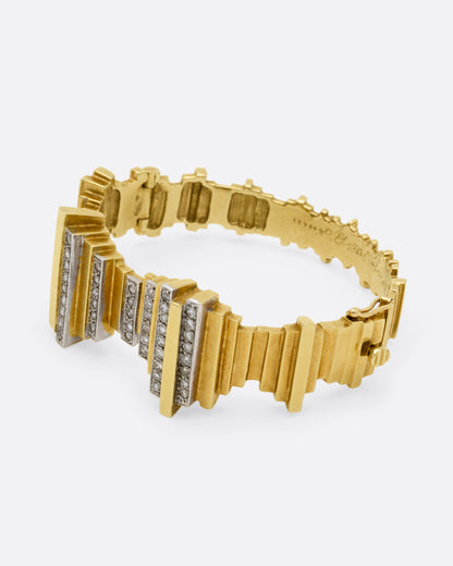 A yellow gold cuff bracelet with queues of diamonds and white gold accents, shown from the side.