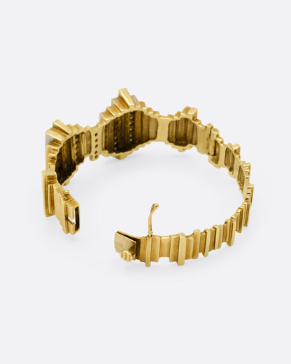 A yellow gold cuff bracelet with queues of diamonds and white gold accents, shown from the back open.