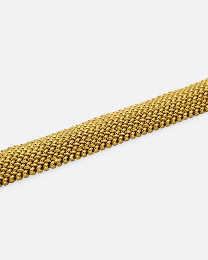 A close up of a wide woven yellow gold bracelet.