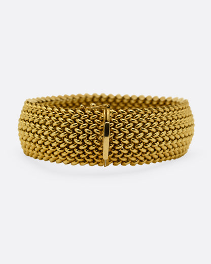 A wide woven yellow gold bracelet, shown from the back.