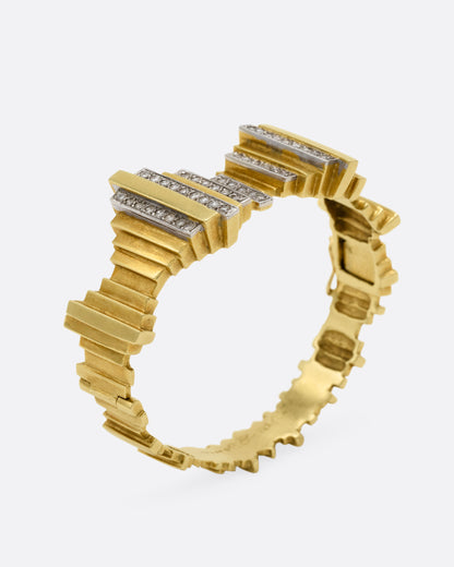 A yellow gold cuff bracelet with queues of diamonds and white gold accents, shown from the side standing up.