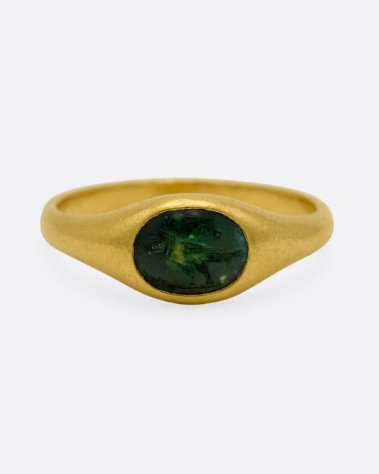 A yellow gold signet ring with a dark green chalcedony carved with a parrot, shown from the front.