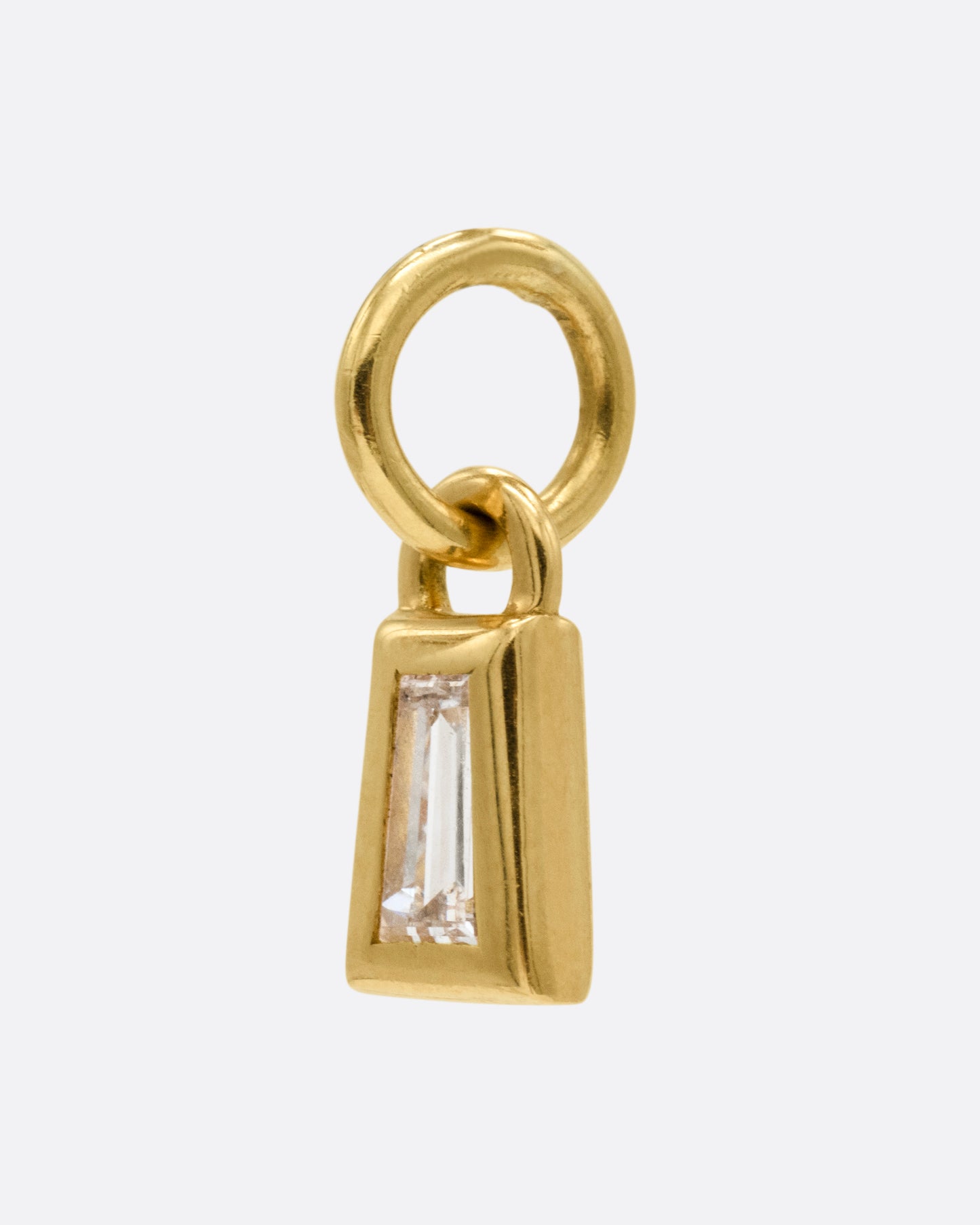 A yellow gold charm with a tapered baguette diamond, shown from the side.
