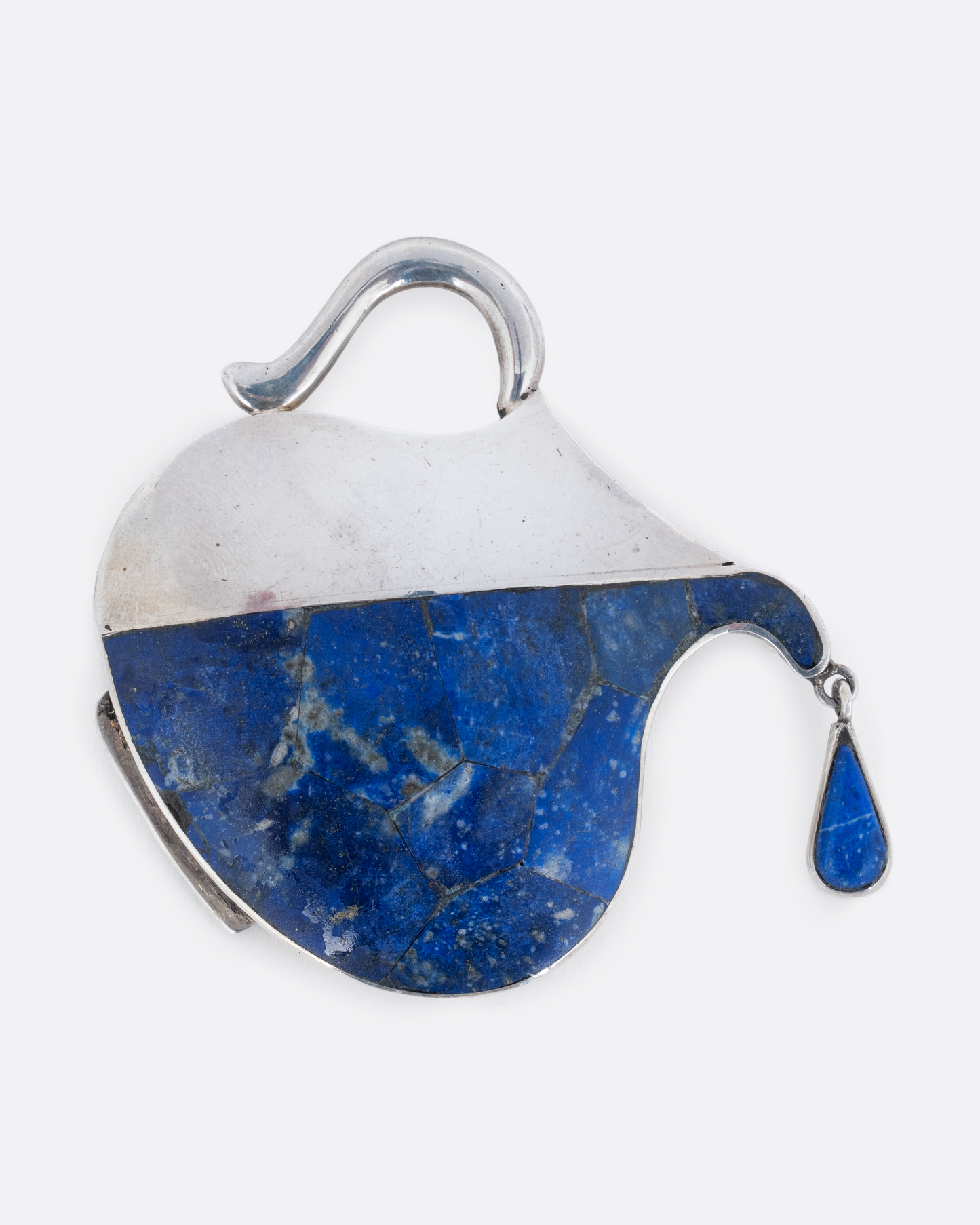 A sterling silver pin in the shape of a pitcher filled with water made of lapis and a dangling drop. Shown from the front, pouring.
