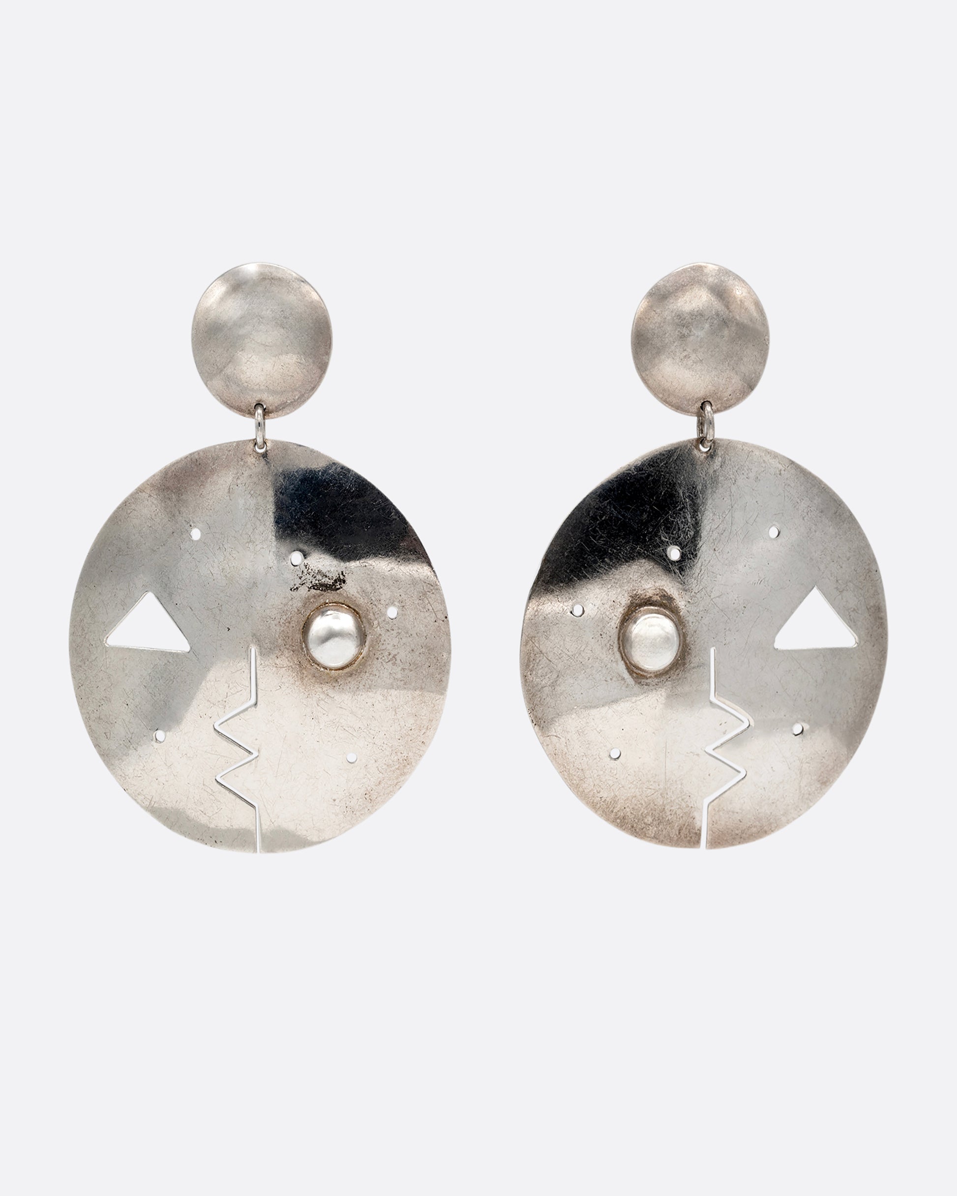 A pair of round drop stud earrings with geometric cutout faces. Shown from the  front.