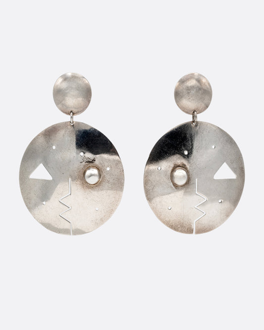 A pair of round drop stud earrings with geometric cutout faces. Shown from the  front.
