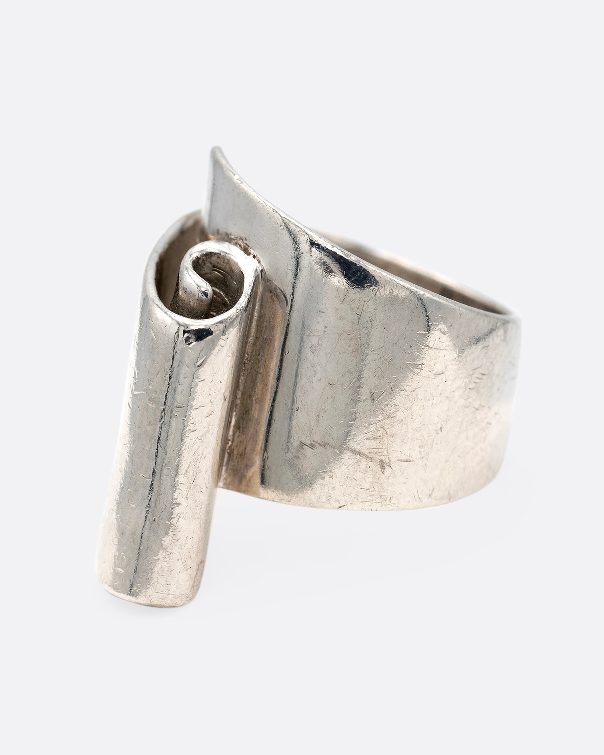 A silver ring with a scroll on its face. Shown from the side.