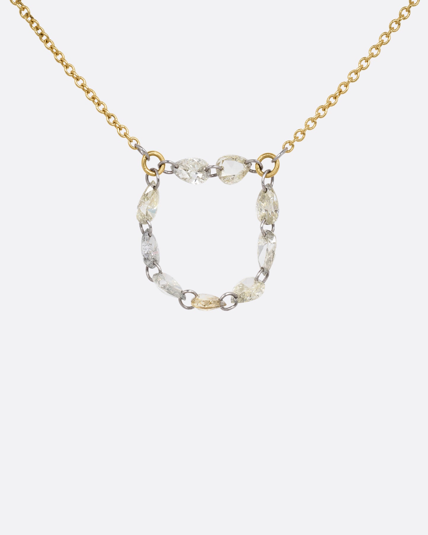 A close up of a yellow gold cable chain necklace with a loop of nine rose cut diamonds at the center. Shown from the front.