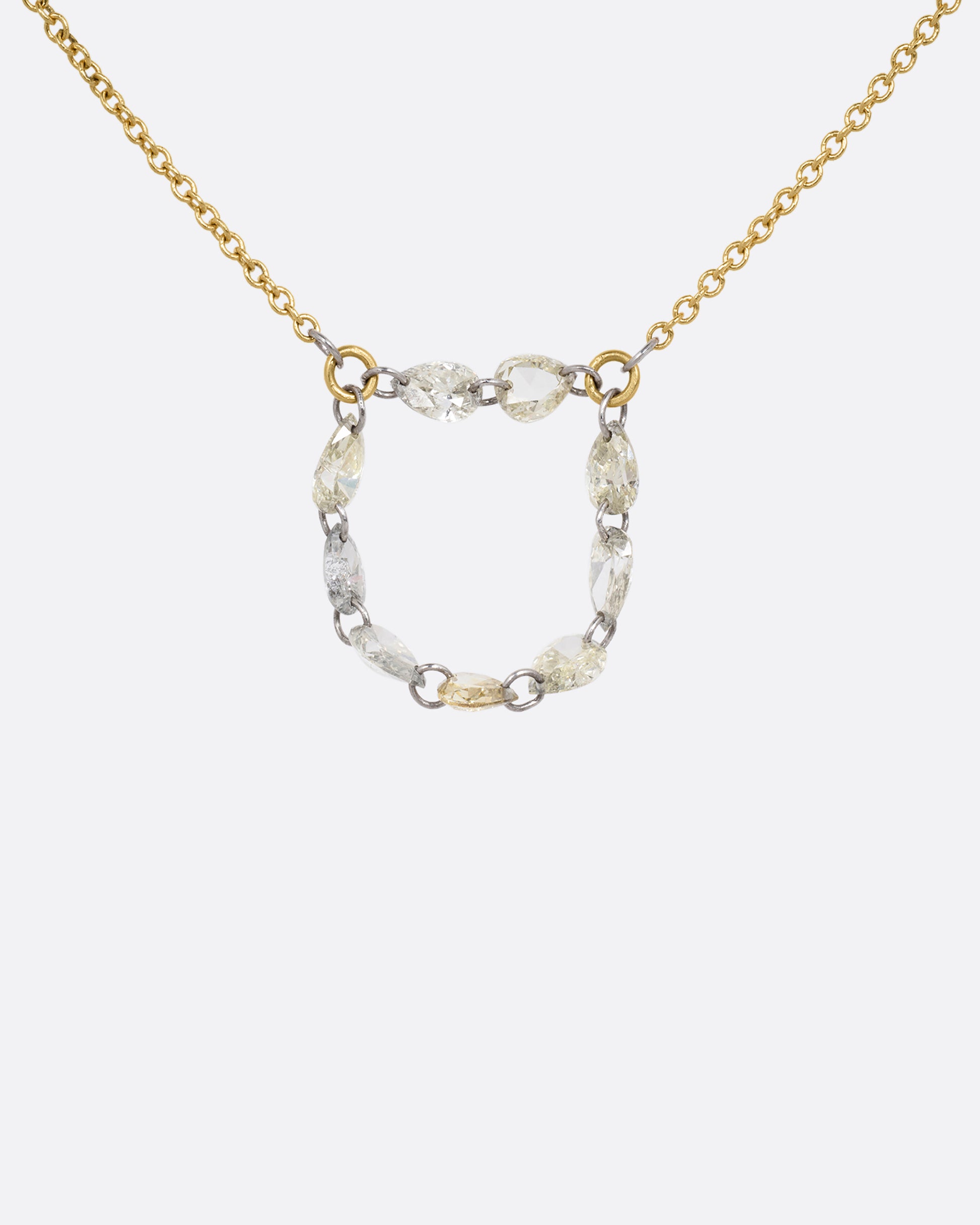 A close up of a yellow gold cable chain necklace with a loop of nine rose cut diamonds at the center. Shown from the front.