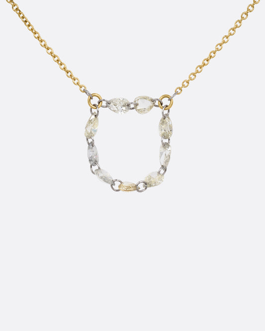 A close up of a yellow gold cable chain necklace with a loop of nine rose cut diamonds at the center. Shown from the front.