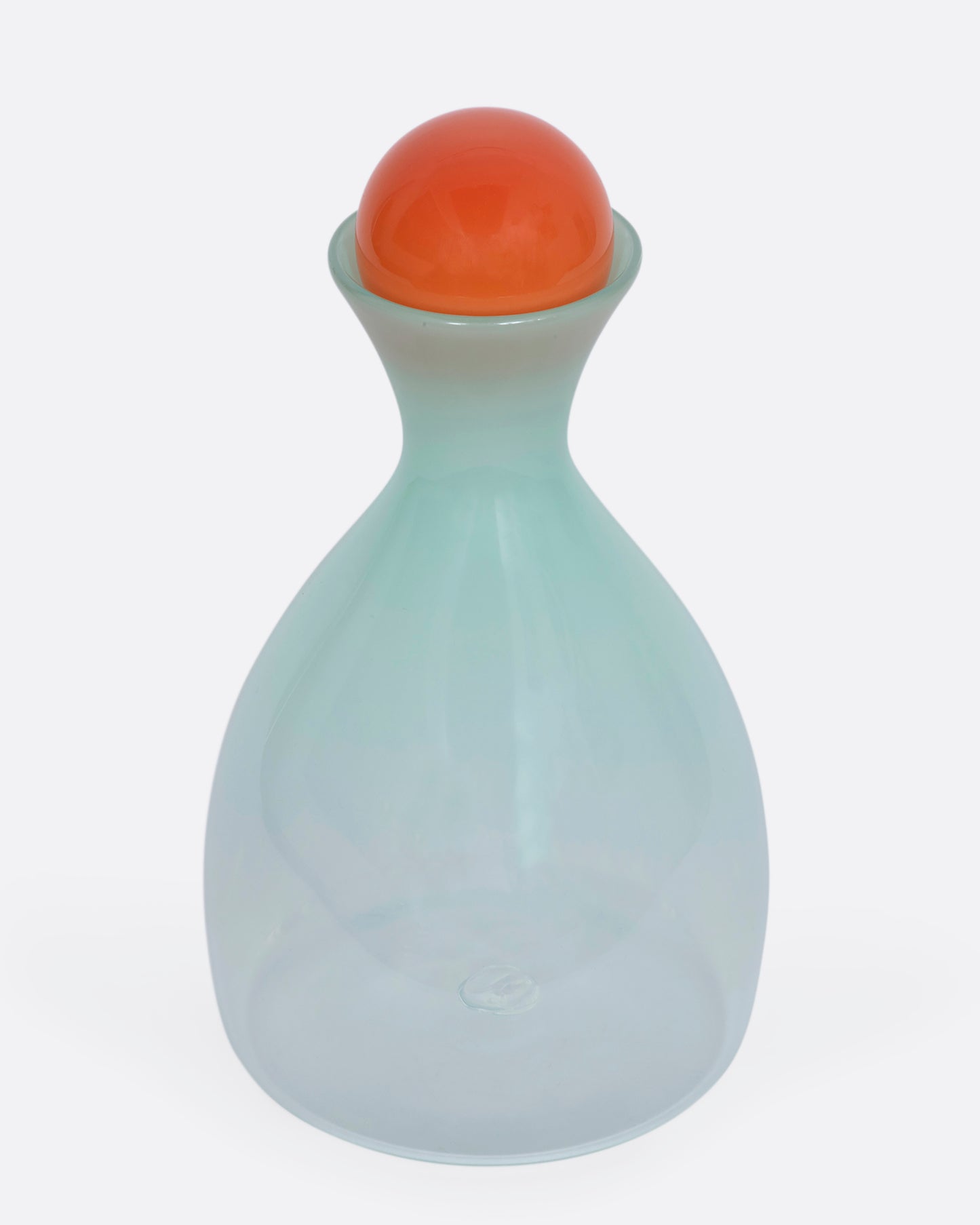 A mint green decanter with an orange sphere stopper. View from the front, slightly above.