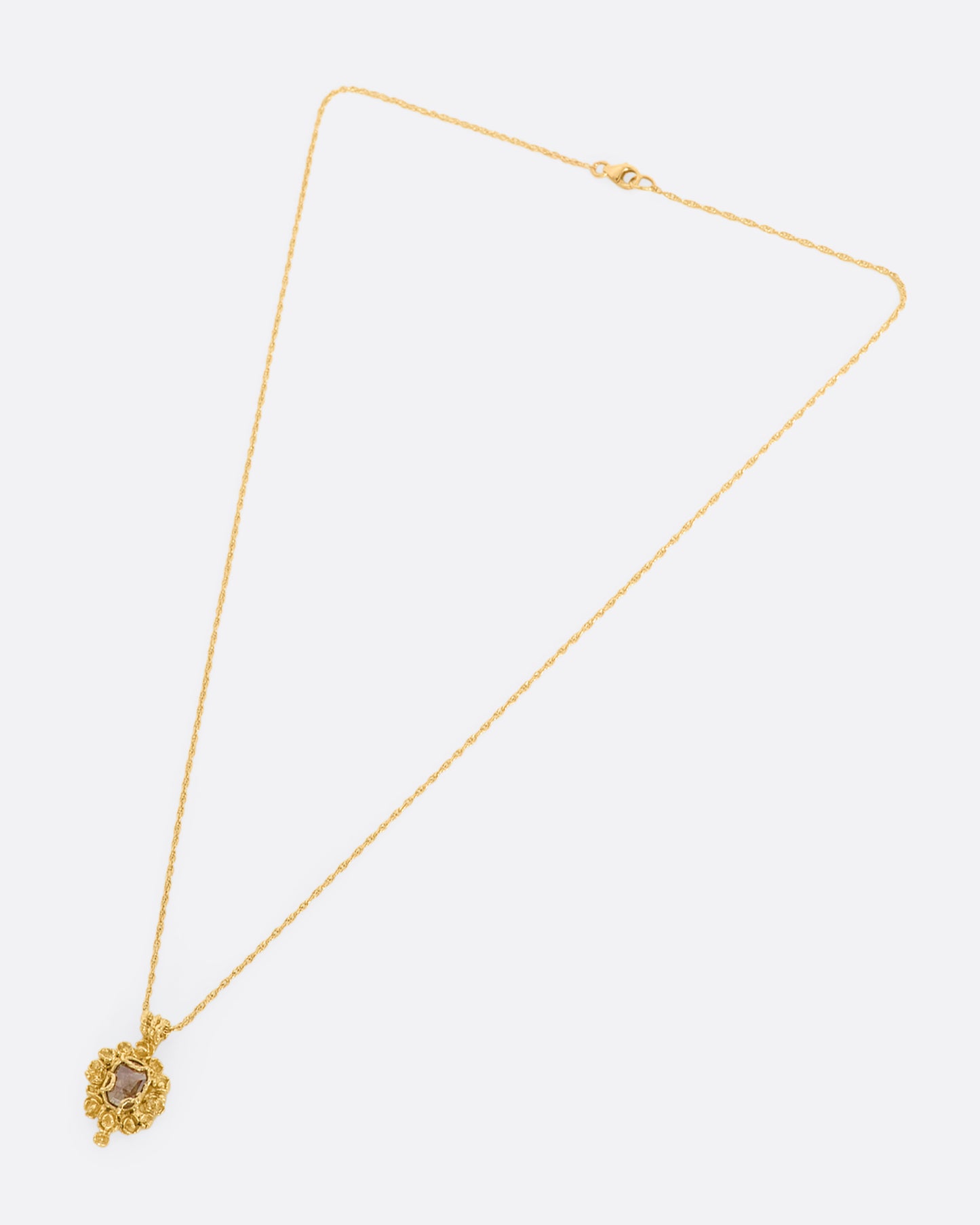 A yellow gold pendant reminiscent of an antique mirror with floral and vine details around an orange rose cut diamond. View from above, laying flat.