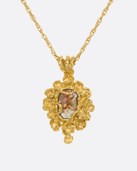 A yellow gold pendant reminiscent of an antique mirror with floral and vine details around an orange rose cut diamond. View from the front.