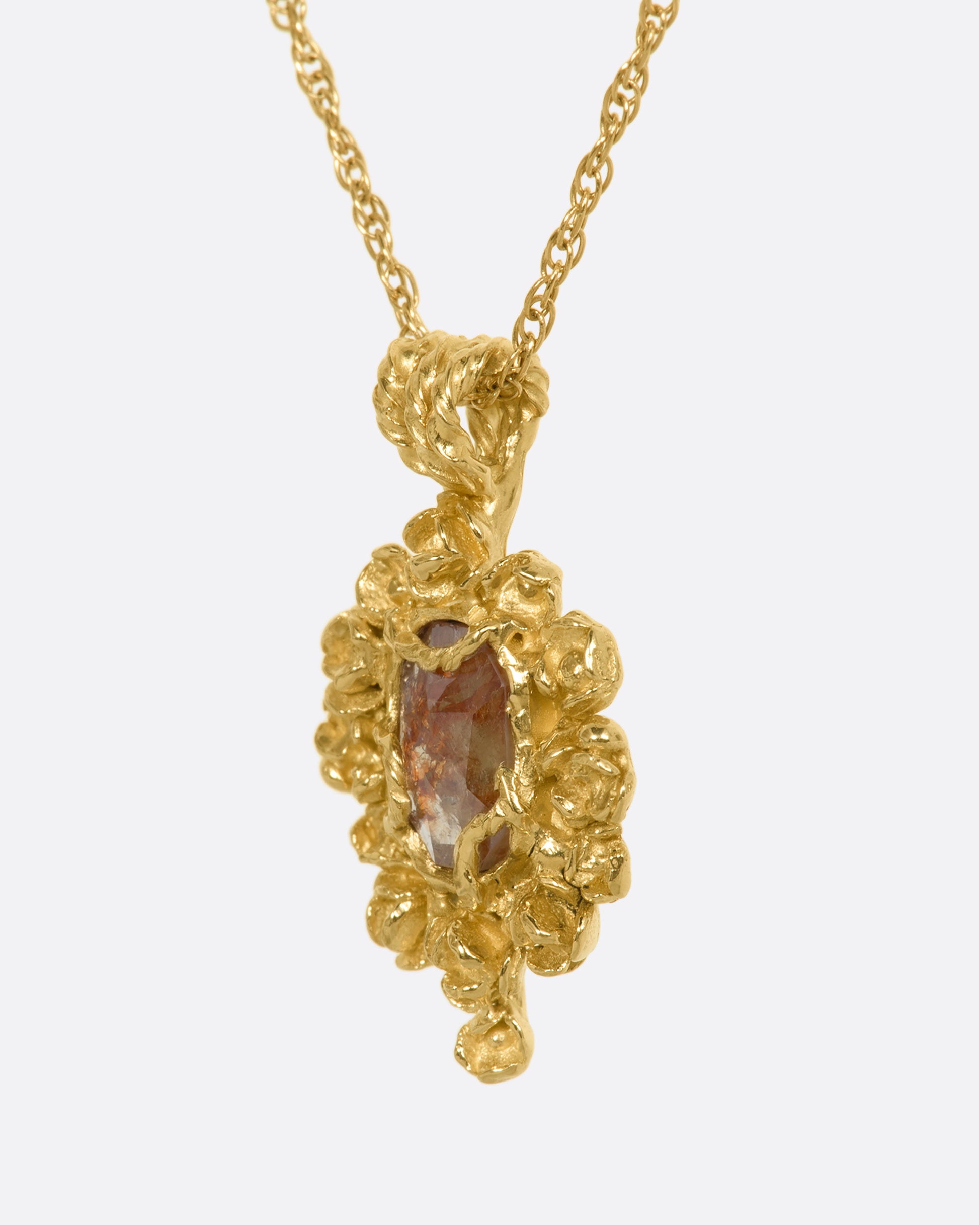 A yellow gold pendant reminiscent of an antique mirror with floral and vine details around an orange rose cut diamond. View from the side.