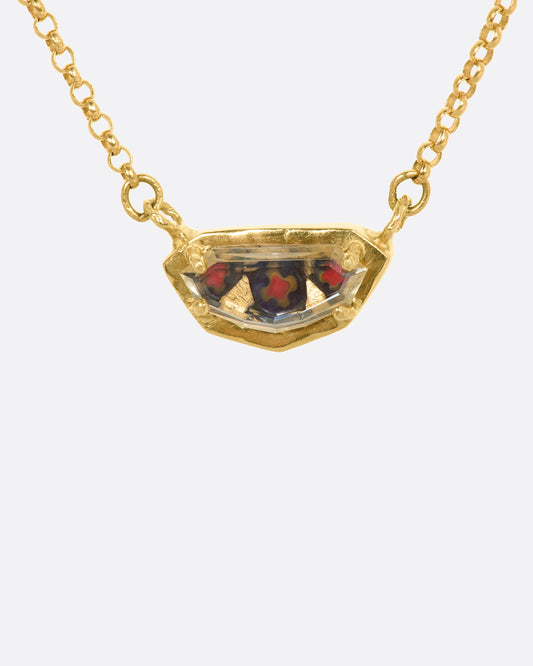 A yellow gold shield shaped necklace with a portrait cut sapphire over micromosaic and goldleaf italian glass and black diamond. View from the front.