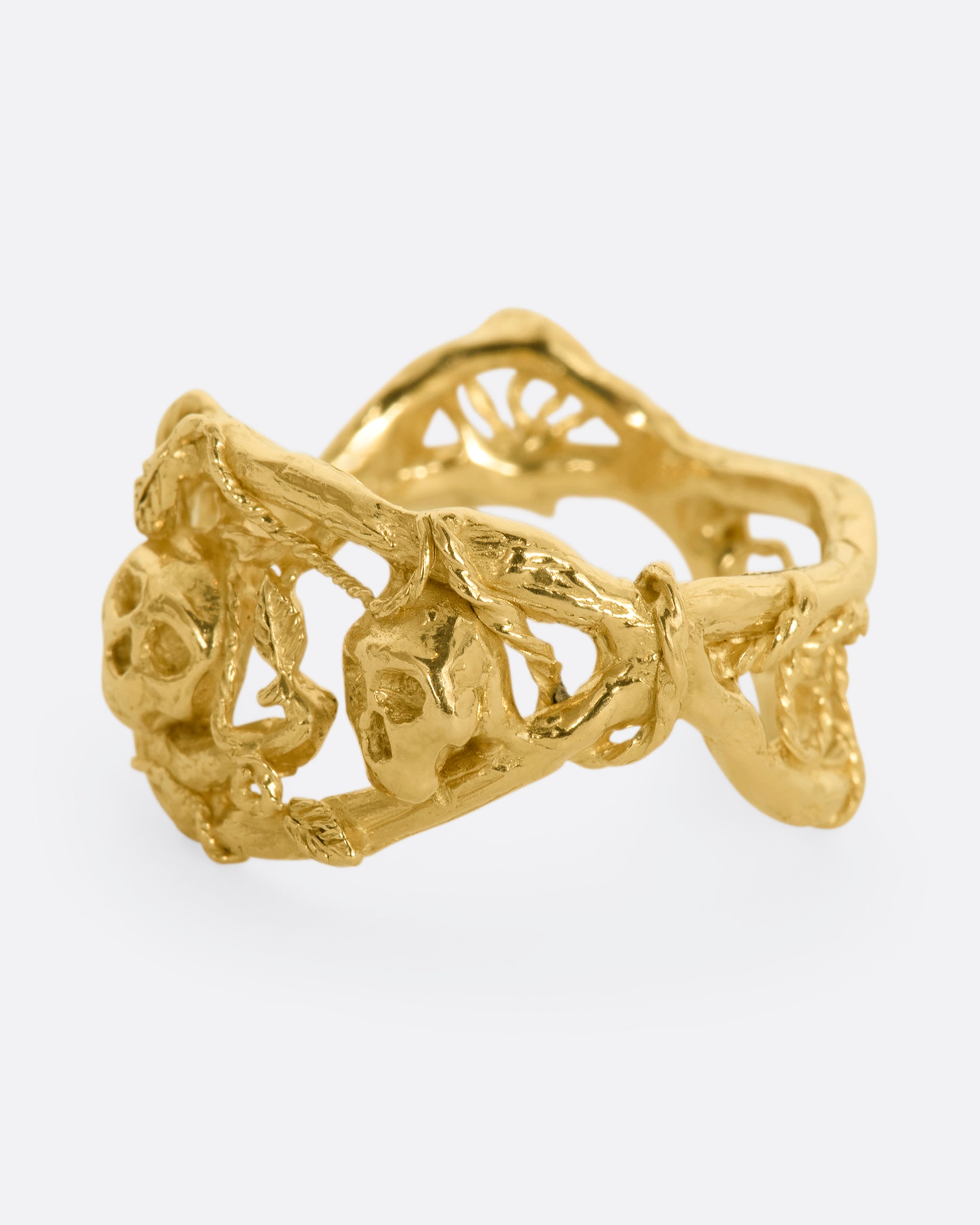 A yellow gold momento mori ring with organic branch and vine motif, featuring two skulls. View from the side.