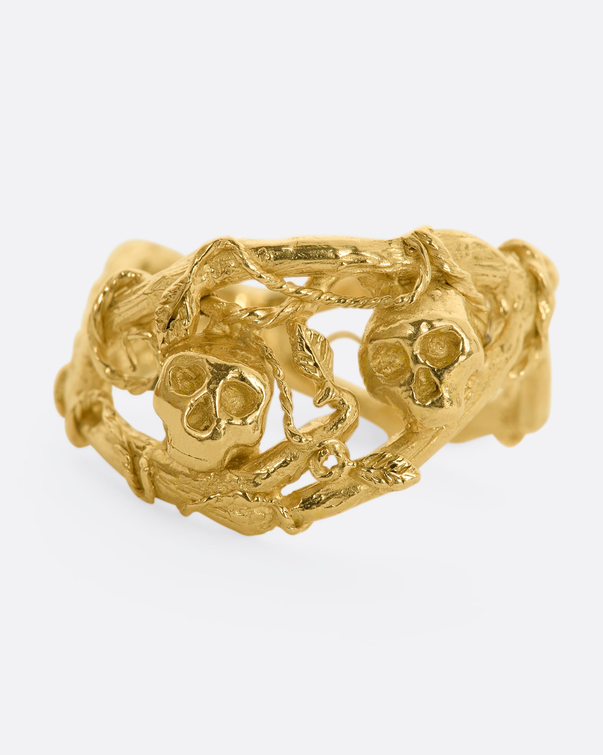 A yellow gold momento mori ring with organic branch and vine motif, featuring two skulls. View from the front.